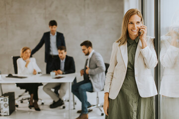 Wall Mural - Young business woman standing in the office and using mobile phone in front of her team