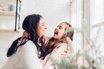 Mother's day. Mother and daughter laughing and hugging on kitchen window sill. Family having fun together at home