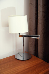 Stylish modern table lamp on a desk near a window with dark curtains