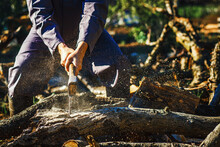Man Holding An Industrial Ax. Ax In Hand. A Strong Man Holds An Ax In His Hands Against The Background Of Chainsaws And Firewood. Strong Man Lumberjack With An Ax In His Hand. Chainsaw Close Up.