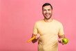 © denis_vermenko - Diet concept. Portrait of man isolated on a pink background holding carrot and apple. Vegetarian preparing a meal. Smiling guy loves fruits and vegetables.