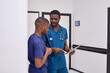 © Roman - Two african american male colleagues doctors working together, discussing and looking at clipboard on clinic
