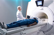 © Roman - Senior Radiologist Controls MRI or CT or PET Scan with Male Patient Undergoing Procedure. High-Tech Modern Medical Equipment. Friendly Doctor Working With Patient