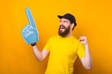 Photo Of Happy Supporter Celebrating And Pointing With Blue Fan Glove Over Yellow Background.