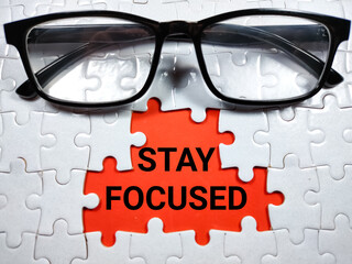 Selective focus.Word STAY FOCUSED with glasses on jigsaw puzzle and red background.Business concept.