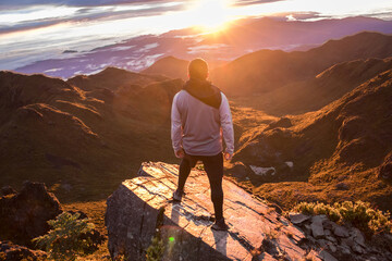 middle aged man looking towards the sunrise after conquering the top of a mountain with a scenic view