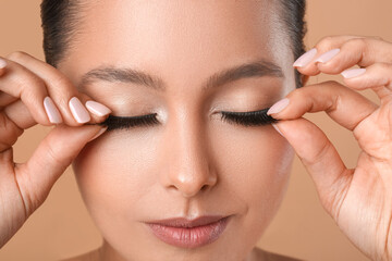 Canvas Print - Beautiful young woman applying fake eyelashes against color background