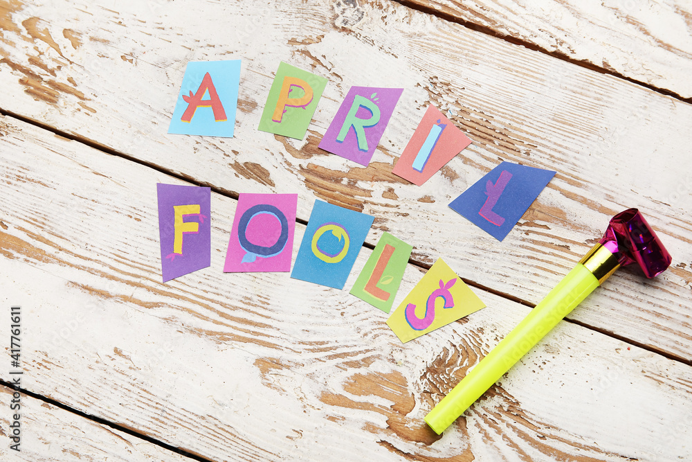 Party horn and text APRIL FOOLS on white wooden background