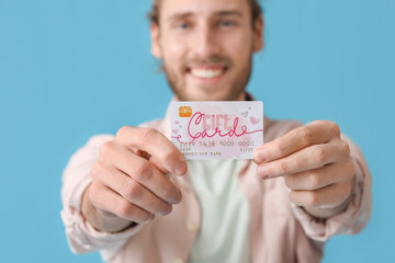 Poster - Handsome young man with gift card on color background, closeup