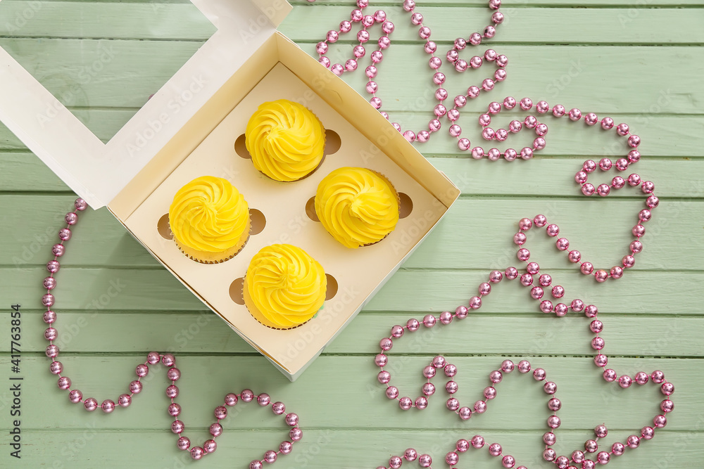 Box with tasty cupcakes on color wooden background
