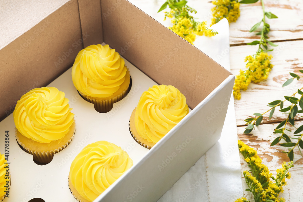 Box with tasty cupcakes and mimosa flowers on table