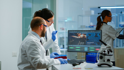 Wall Mural - team medical scientist conducting dna experiments looking in computer holding test tube with blood s