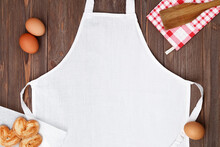 Blank White Apron Template On Wooden Table With Cookies And Eggs, Copy Space. Kitchen, Cooking Clothing Mockup