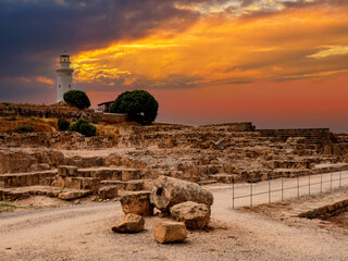 Canvas Print - Cyprus on a summer evening. Pathos on background of evening sunset. White lighthouse next to tomb of kings. Lighthouse on Mediterranean Sea coast. Sights of city of Pathos.Tours in Cyprus