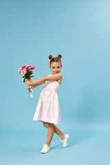 adorable smiling little girl holding bouquet of roses isolated on blue studio background. child gives bouquet to mom. mothers day