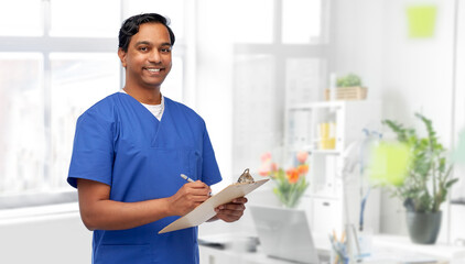 Poster - healthcare, profession and medicine concept - happy smiling indian doctor or male nurse in blue uniform writing report on clipboard over medical office at hospital background