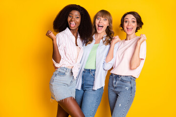 Wall Mural - Photo of three delighted pretty girls dark skin fists up open mouth scream yeah isolated on yellow color background