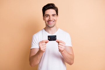 Canvas Print - Portrait of satisfied young person toothy smile hands holding banking card isolated on beige color background