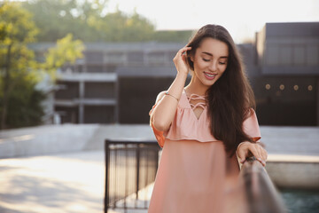 Sticker - Beautiful young woman in stylish pink dress near railing outdoors