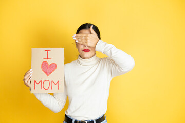 Beautiful woman celebrating mothers day holding poster love mom message serious and covering her eyes with her hand