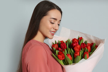 Wall Mural - Happy woman with red tulip bouquet on light grey background. 8th of March celebration