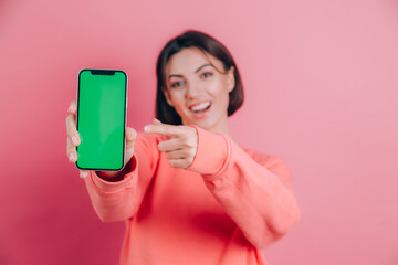 Look at this cell phone! Pleased happy woman points with index finger at blank screen, shows modern device, happy surprised emotions.