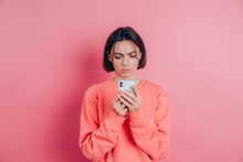 Young Woman Is Feeling Sad Unhappy Angry While Reading Sms Using Her Mobile Phone, Over Pink Background