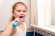 © andrei310 - Little girl brushes her teeth with an electric toothbrush in the morning in the bathroom