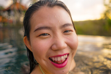 Wall Mural - young woman relaxed at luxury resort infinity pool - happy and cheerful Asian Korean girl taking selfie photo in bikini enjoying jungle view at hotel swimming pool during summer holidays