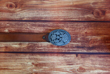 Leather Cowboy Belt With Oval Patterned Buckle On A Wooden Background