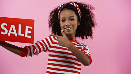 happy african american girl pointing with finger at sale letting isolated on pink