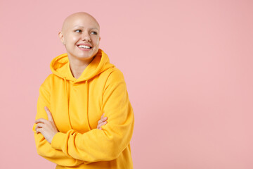 Young bald smiling caucasian cheerful friendly nice woman 20s without hair wear yellow casual sweatshirt shirt hold hands folded crossed look aside isolated on pastel pink background studio portrait.