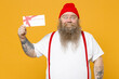 Fat pudge obese chubby overweight tattooed bearded surprised caucasian man 30s has big belly in white t-shirt red hat suspenders hold gift voucher flyer mock up isolated on yellow background studio.