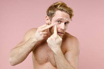 Wall Mural - Worried bearded naked young man 20s years old perfect skin playing with his face looking camera isolated on pastel pink background studio portrait. Skin care healthcare cosmetic procedures concept.