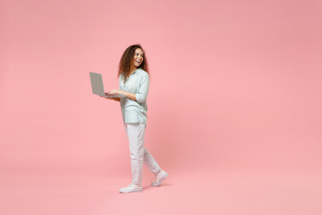 Wall Mural - Full length young black african fun happy smiling curly student woman 20s wearing blue shirt hold laptop pc computer walking looking aside isolated on pastel pink color background studio portrait.