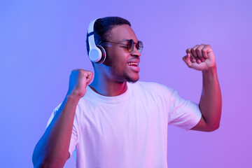 Wall Mural - Handsome Black Guy Listening Music In Wireless Headphones And Dancing, Neon Lighting