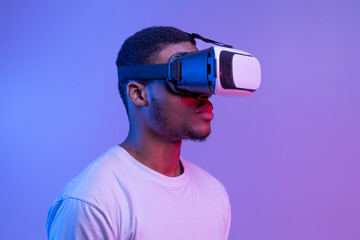 Wall Mural - Black Man In VR Headset Standing In Neon Light Over Purple Background