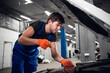 © Anna Kosolapova - A mechanic using tools to repair a car engine. He is dressed in overalls