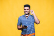 © VISTA by Westend61 - Smiling handsome man wearing headphones while holding mobile phone against yellow background