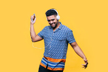 Smiling Man With Mobile Phone Dancing While Listening Music Through Headphones Against Yellow Background