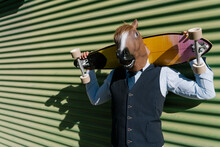 Businessman In Horse Mask Holding Longboard Behind Head Against Wall