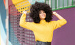 © VISTA by Westend61 - Curly hair woman smiling while standing against multi colored wall