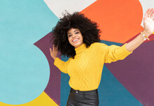 Young Woman With Arms Outstretched Smiling While Dancing Against Colorful Wall