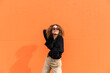 © VISTA by Westend61 - Young woman wearing sunglasses dancing while standing against orange wall