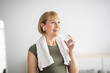 © Prostock-studio - Wellness and healthy lifestyle. Positive mature lady with glass of fresh clear water after sports workout indoors