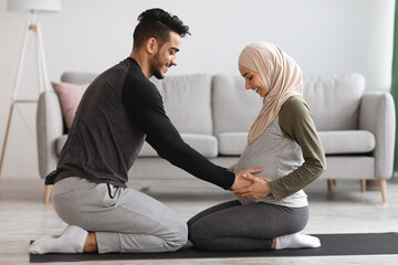 Wall Mural - Caring Arab Husband Touching Pregnant Belly Of His Wife In Hijab At Home