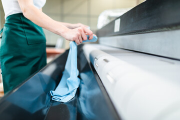 Wall Mural - Young laundry worker pats the linen on the automatic machine at the dry cleaners.