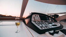 A Wide-angle View Of The Interior Of A Luxury Cruising Yacht In A Wheelhouse With A Dashboard And A Selective Focus On A Glass Of Champagne Standing Near The Window With A Dramatic Sunset Evening Sky