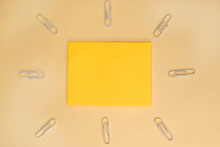 On A Yellow Background Among White Paper Clips Is A Yellow Blank Sheet For Notes