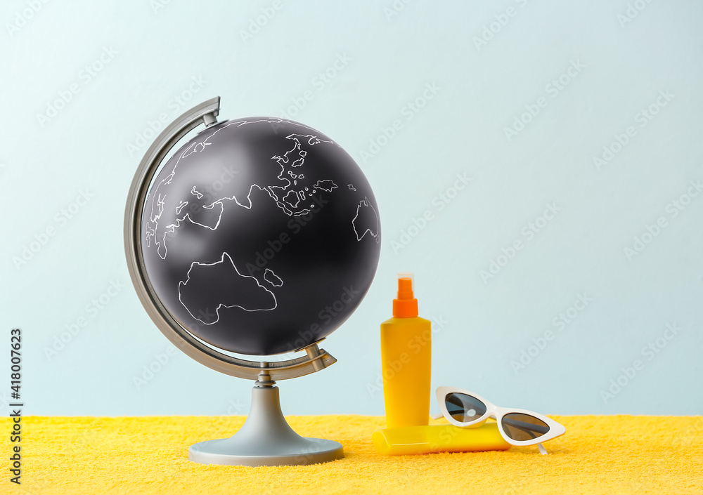 Globe with sunglasses and sunscreen on color background